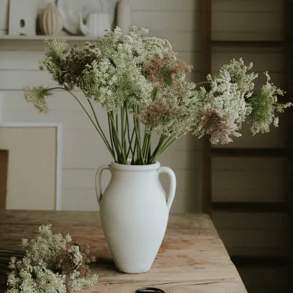 Kwiaty Dzika marchew 'Dara' w białym ceramicznym wazonie na rustykalnym drewnianym stole, z bukietem, nożyczkami i wystrojem półki w butiku.