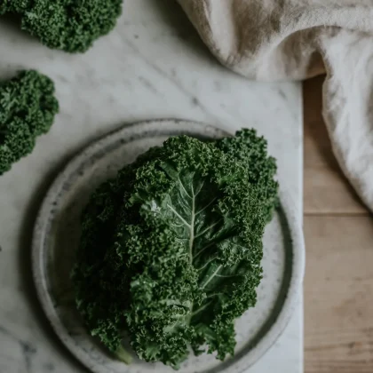 Wysokiej jakości liście jarmużu 'Westland Autumn' wyeksponowane na szarym ceramicznym talerzu, idealne do ogrodu, na marmurze z beżową tkaniną.