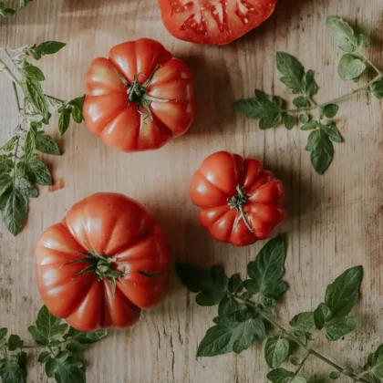 Pomidory malinowe Marmande na rustykalnej drewnianej powierzchni - świeże zielone liście i plasterki dla butiku ogrodniczego Organic Gardening.