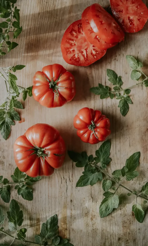 Pomidory malinowe Marmande na rustykalnej drewnianej powierzchni - świeże zielone liście i plasterki dla butiku ogrodniczego Organic Gardening.