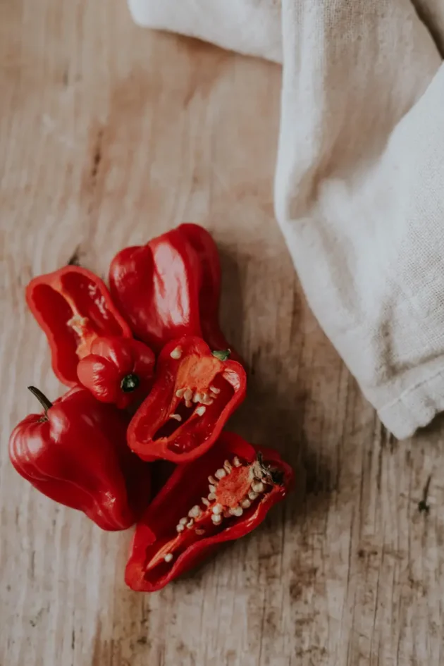 Świeża czerwona papryka chili Habanero Red i pokrojona czerwona papryka z nasionami na rustykalnym drewnianym tle dla internetowego butiku ogrodniczego. Naturalny lekki akcent materiałowy w rogu. Odkryj ekologiczne niezbędne produkty ogrodnicze i żywe rośliny warzywne tutaj.