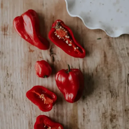 Żywe, różnorodne czerwone papryczki chili Habanero Red na rustykalnym drewnianym tle - internetowy butik ogrodniczy. Całe i połówki papryczek chili z nasionami na falistym białym talerzu w rogu. Idealne dla miłośników pikantnych ogrodów!.