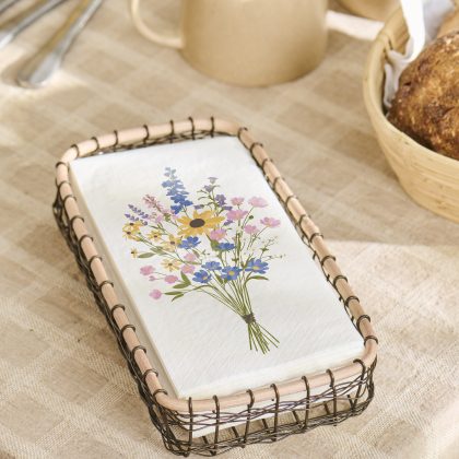 Serwetki Wildflower Serwetki "Letni bukiet" w drucianym koszyku na obrusie w kratkę, z filiżankami, sztućcami i dekoracją z ogródka chlebowego.