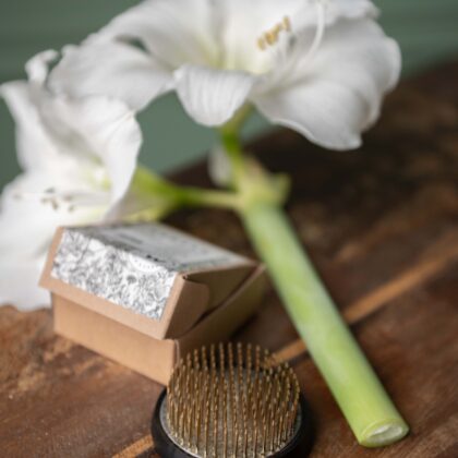 Biały kwiat amarylis na drewnianej powierzchni z otwartym pudełkiem, papierem kwiatowym i żabką kwiatową Kenzan S (Kopia) do układania kwiatów.