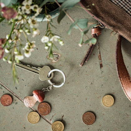 Ręcznie wykonany breloczek Drewniany Grzybek z kluczami, monetami euro, paskiem do torebki i świeżymi białymi kwiatami ogrodowymi na kamieniu.