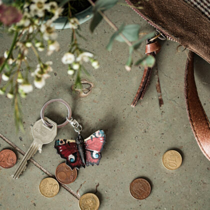 Drewniany breloczek Grzybek o tematyce ogrodowej na zielonej powierzchni, z białymi kwiatami, zielonymi liśćmi, monetami i skórzaną torbą.