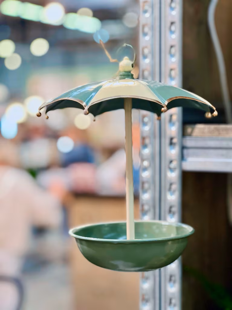 Zielony karmnik dla ptaków Karmnik Parasol z osłoną parasolową zdobi metalową półkę, idealną do stylowych ekspozycji w ogrodzie.