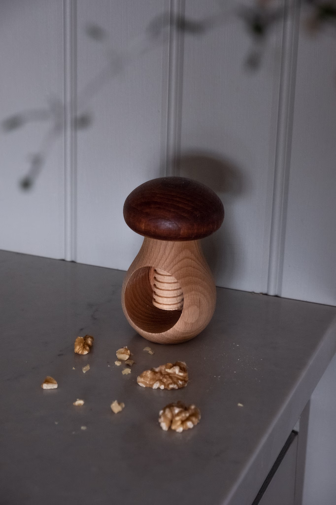 Dziadek do orzechów w kształcie grzybka Drewniany Grzybek na szarym blacie z orzechami włoskimi, idealny prezent dla miłośników ogrodów, rustykalne tło dekoracyjne.