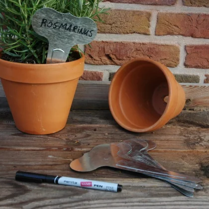 metalowa etykieta do roślin, pustymi doniczkami i długopisem na drewnie przy ceglanej ścianie.