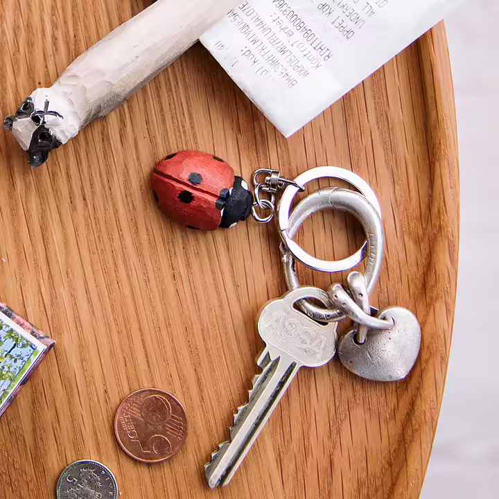 Drewniany Breloczek Biedronka dla miłośników ogrodów, na srebrnych kluczykach z serduszkiem, wyeksponowany na drewnie obok paragonu i monety.